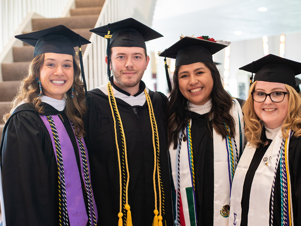 Four Gustavus students posing for a photo in their cap and gown at graduation in Christ Chapel.